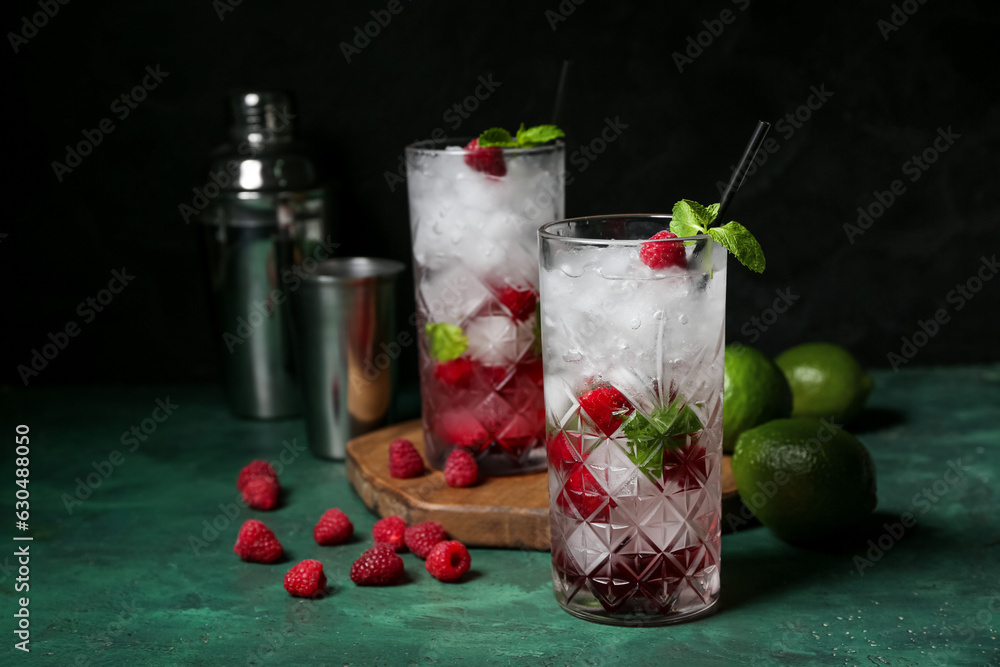 Wooden board with glasses of fresh raspberry mojito and limes on green table