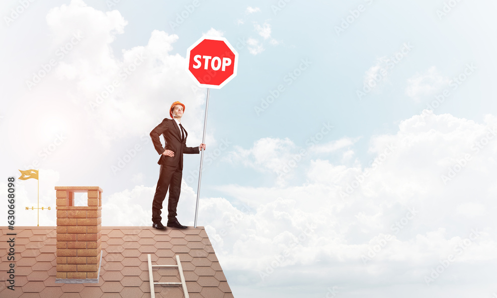 Caucasian businessman on brick house roof showing stop road sign. Mixed media