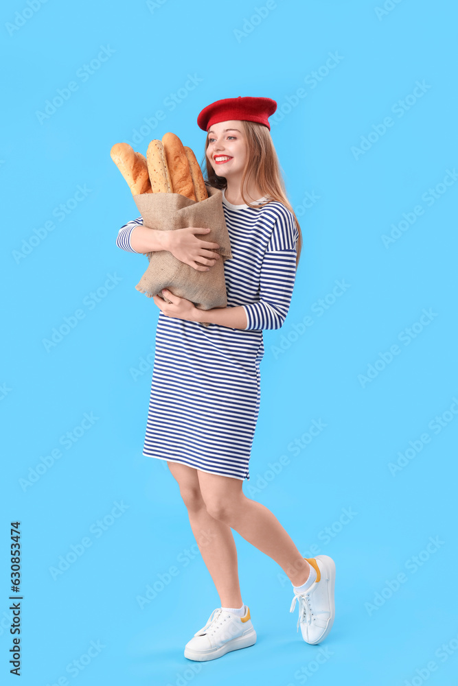 Young woman in beret with sack bag of fresh baguettes on blue background