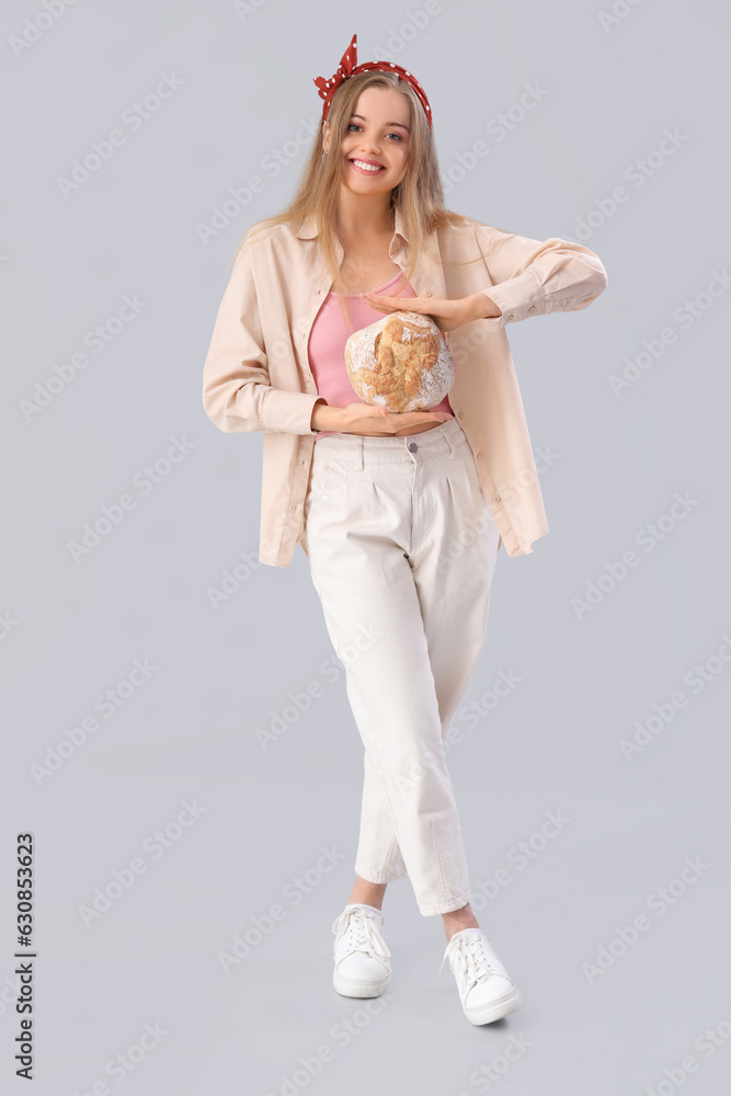 Young woman with fresh bread on grey background