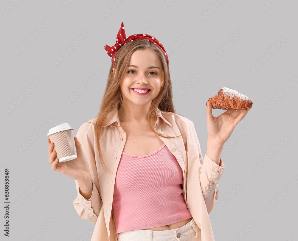 Young woman with tasty croissant and cup of coffee on grey background