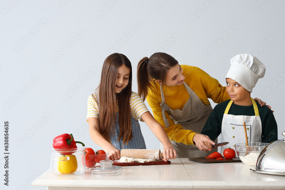 Female chef with little children during cooking class on light background