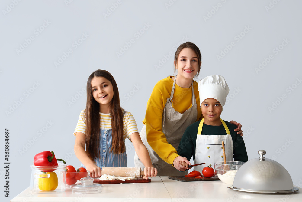 Female chef with little children during cooking class on light background