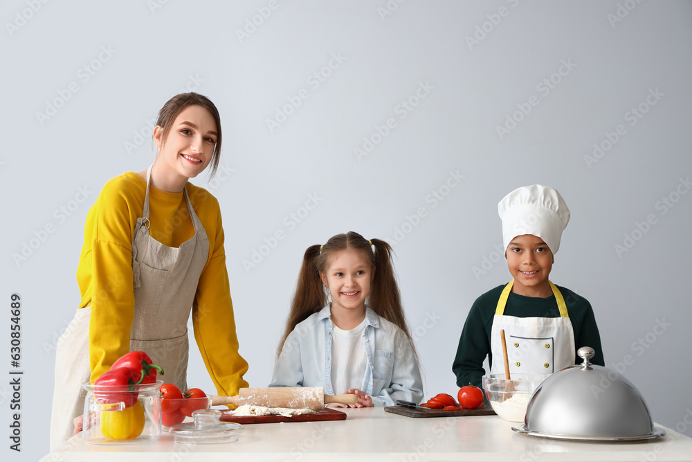 Female chef with little children during cooking class on light background