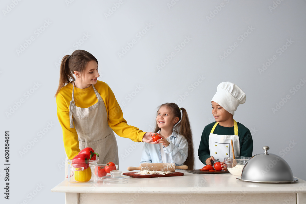 Female chef with little children during cooking class on light background