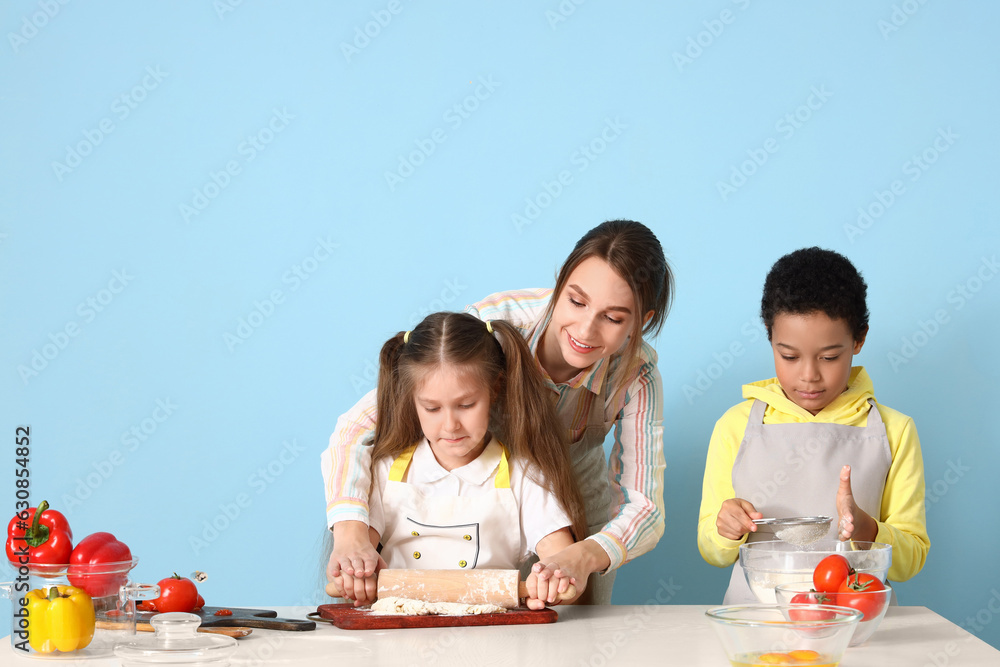 Female chef with little children during cooking class on blue background