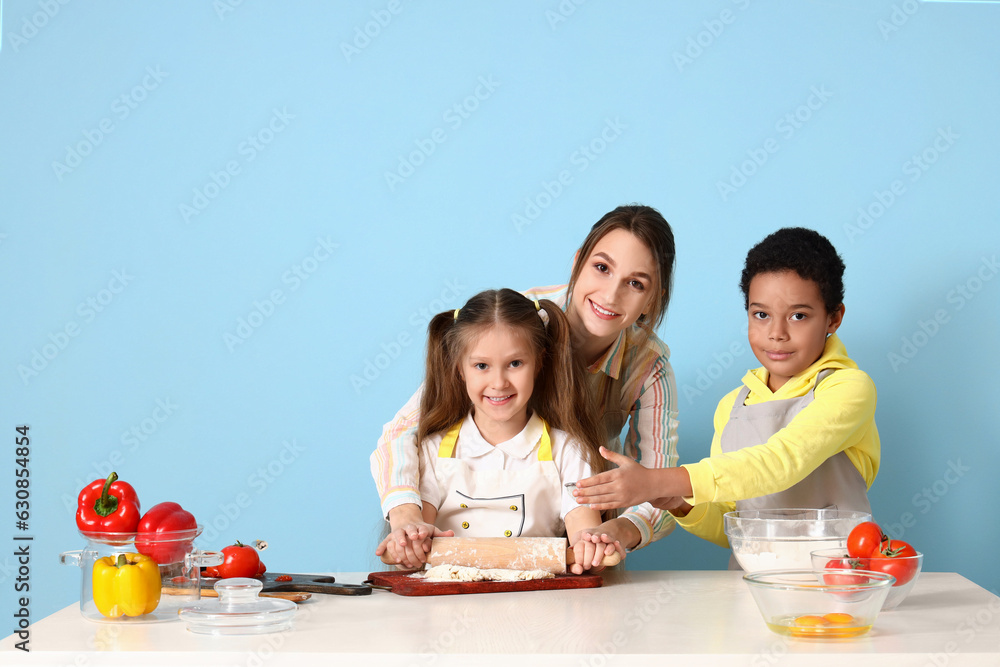 Female chef with little children during cooking class on blue background