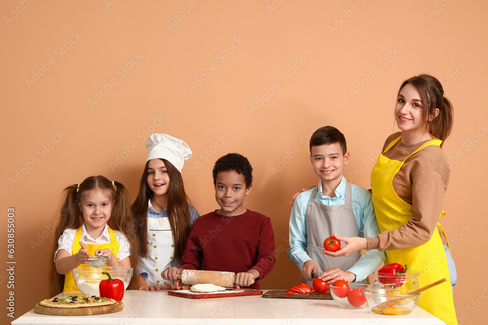 Female chef with group of little children during cooking class on beige background