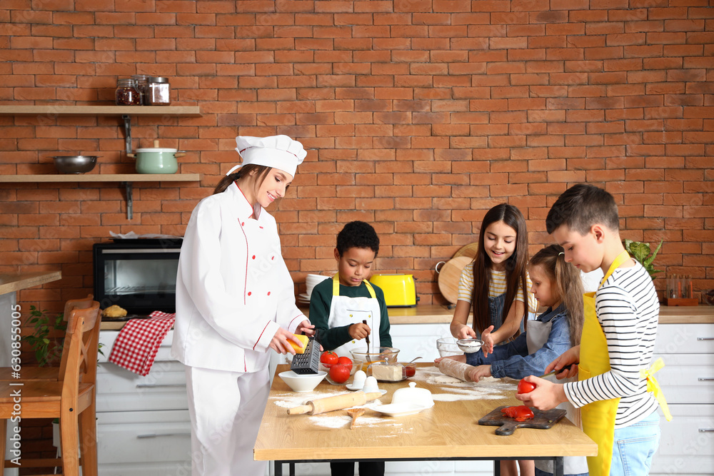 Female chef with group of little children preparing pizza during cooking class in kitchen