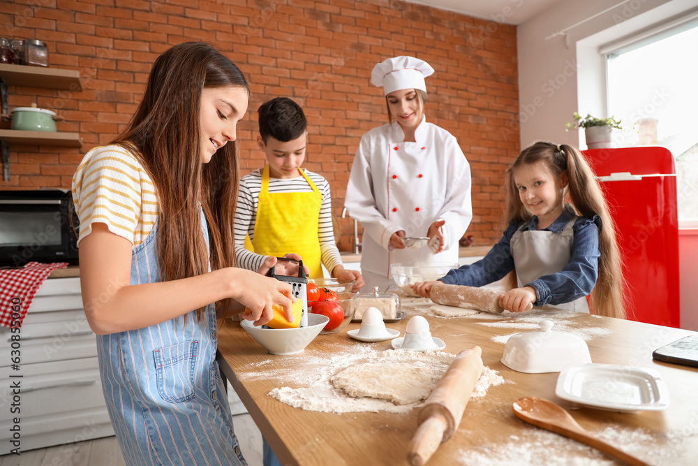 Female chef with group of little children preparing pizza during cooking class in kitchen