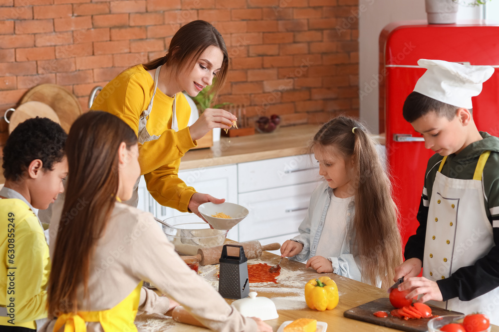 Female chef with group of little children preparing pizza during cooking class in kitchen