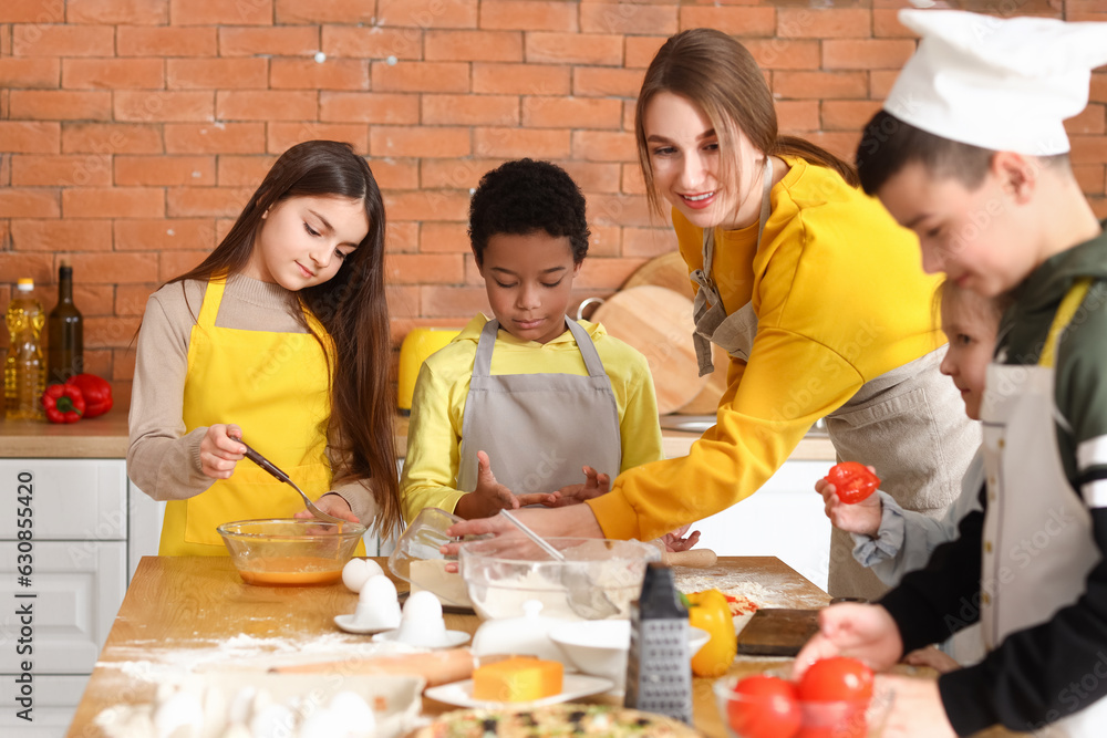 Female chef with group of little children preparing pizza during cooking class in kitchen