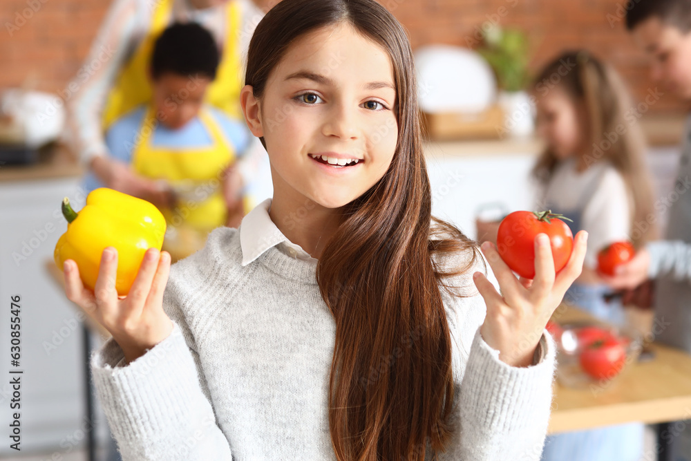 Little girl with vegetables during cooking class in kitchen