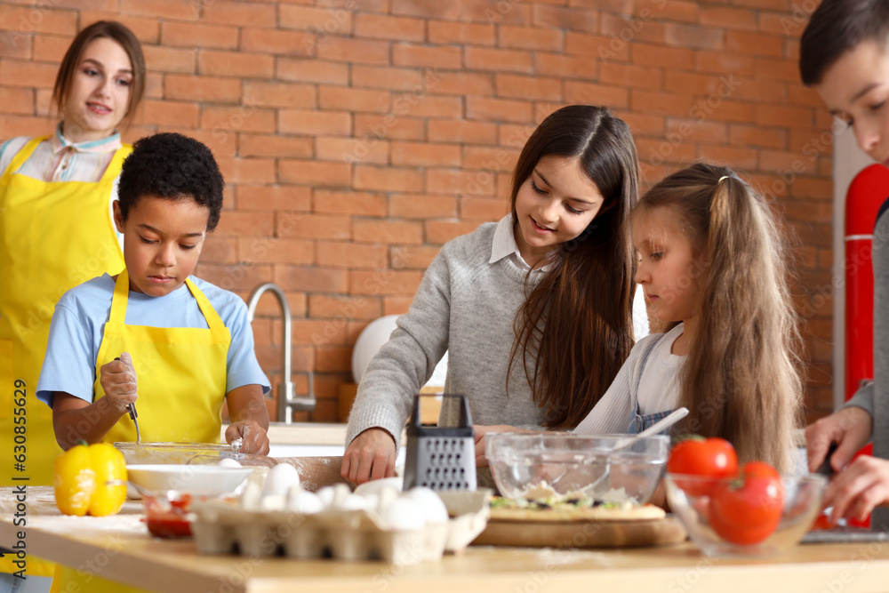 Little children preparing pizza during cooking class in kitchen