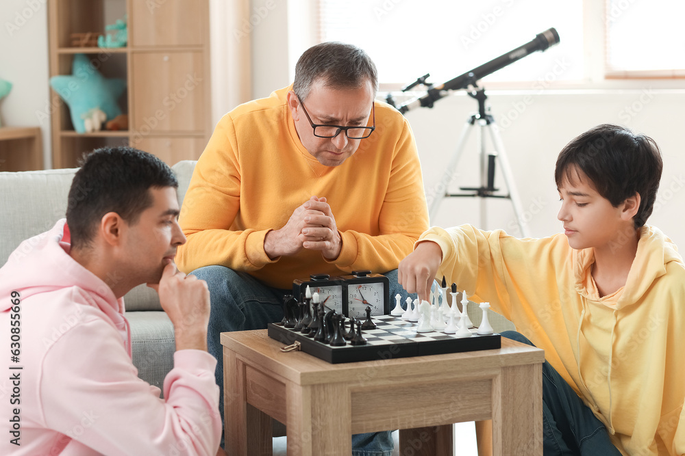 Happy little boy with his dad and grandfather playing chess at home