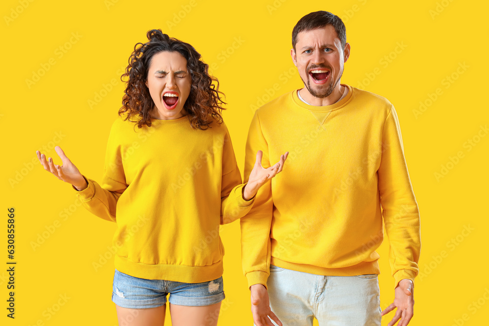 Angry young couple on yellow background