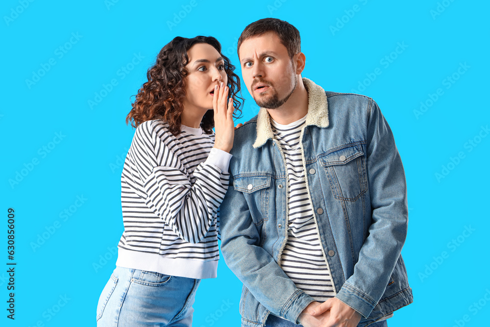 Young woman telling her husband secret on blue background