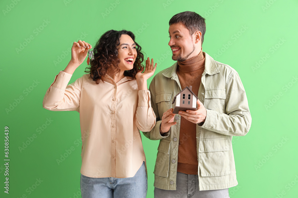 Happy young couple with house model and keys on green background