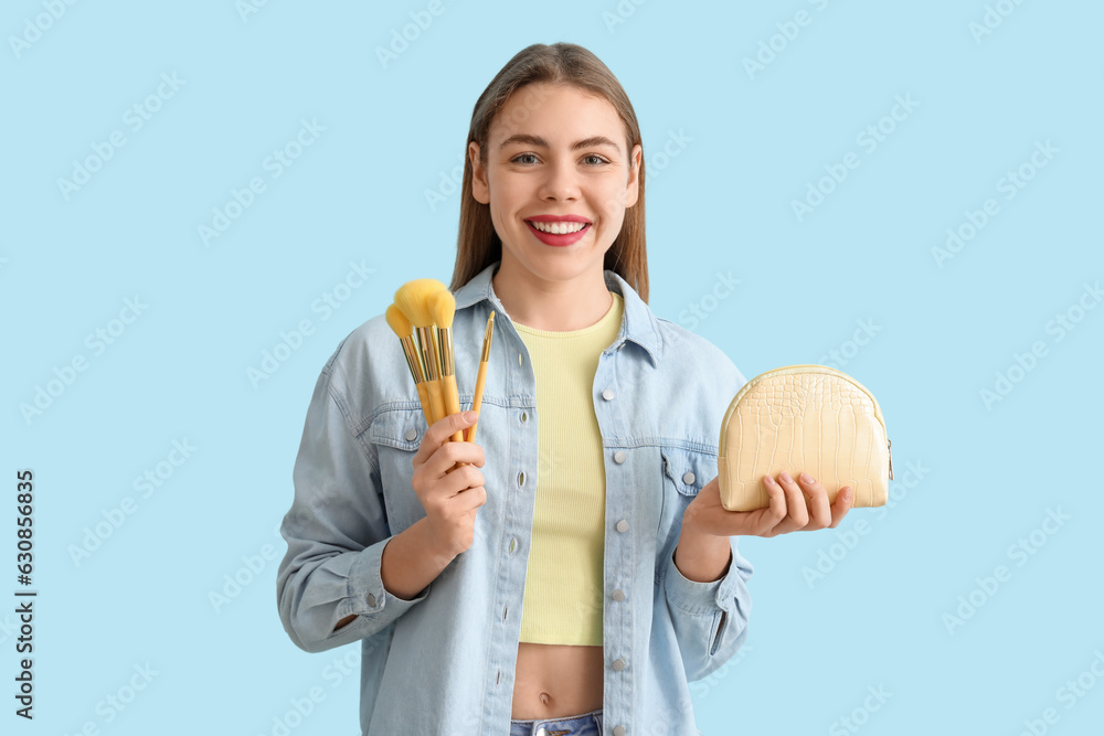 Young woman with cosmetic bag and makeup brushes on blue background