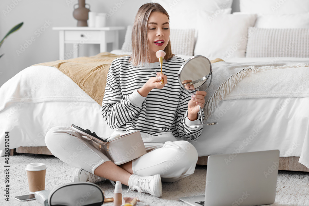 Young woman with mirror applying powder in bedroom