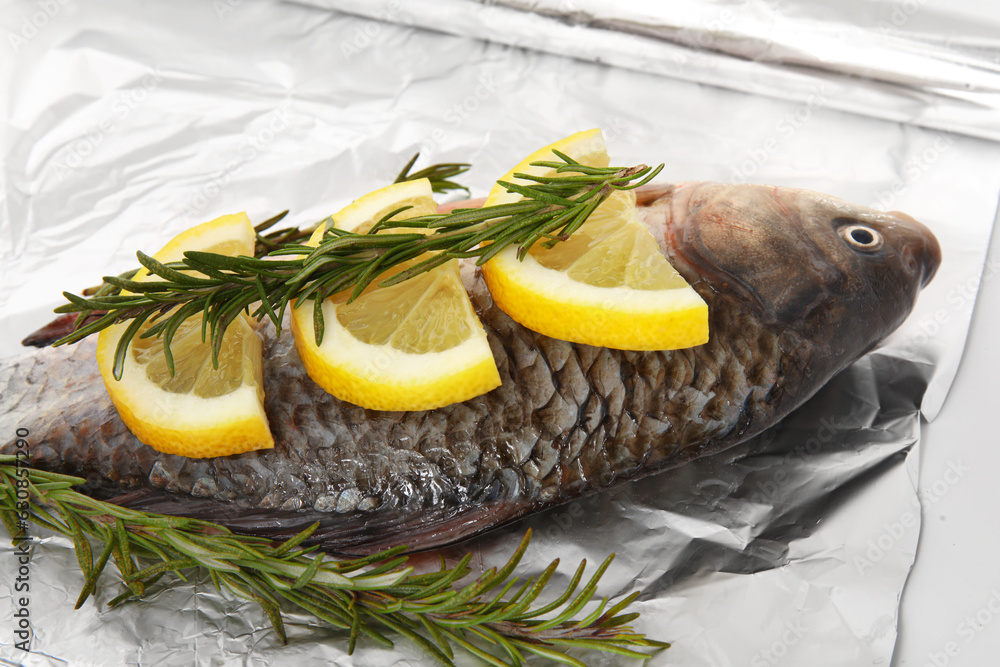 Aluminium foil roll with raw fish, lemon slices and rosemary, closeup