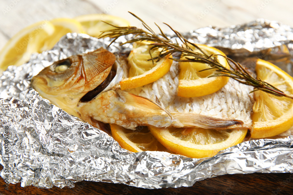 Aluminium foil with tasty baked fish, lemon slices and rosemary, closeup