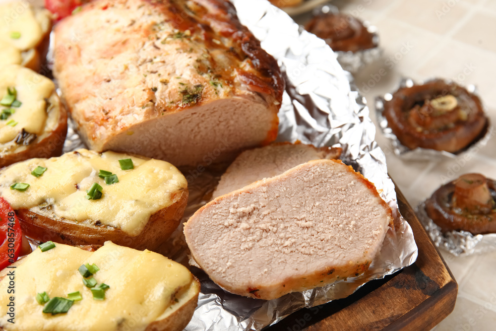 Wooden board with tasty baked meat and potatoes, closeup