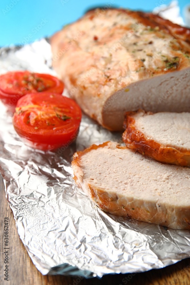 Aluminium foil with tasty baked meat and tomatoes, closeup