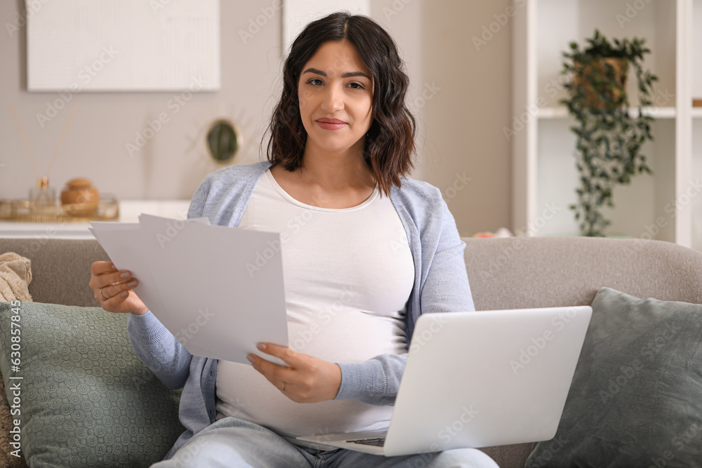 Young pregnant woman working with documents and laptop at home