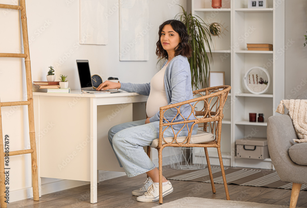 Young pregnant woman working with laptop at table in office