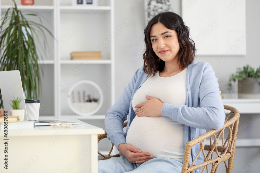 Young pregnant woman working at table in office