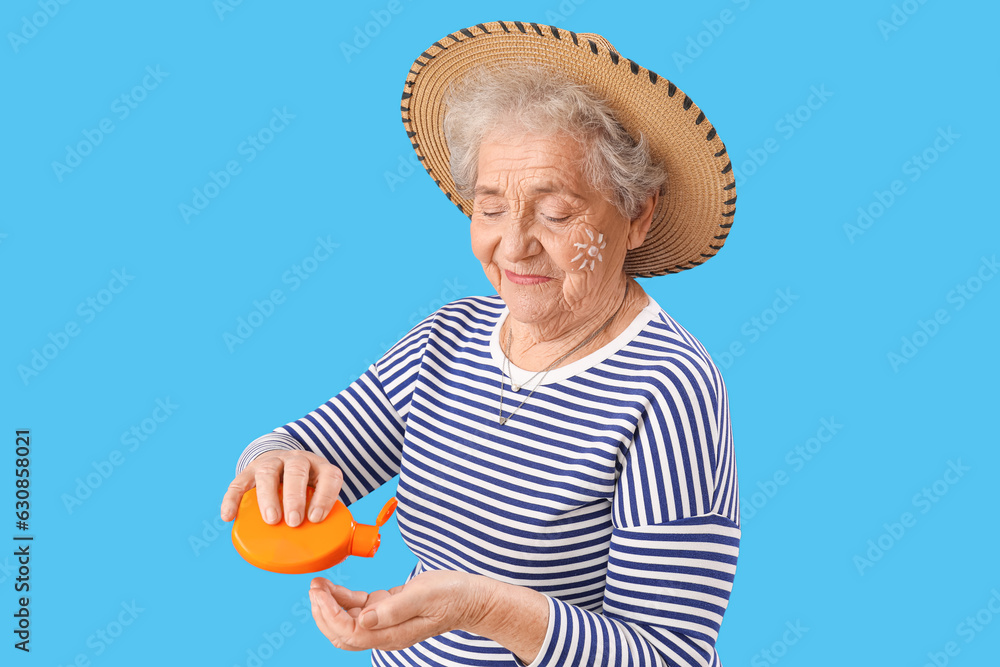 Senior woman applying sunscreen cream on blue background