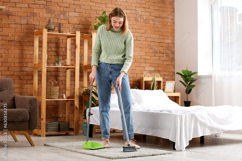 Young woman sweeping floor in bedroom