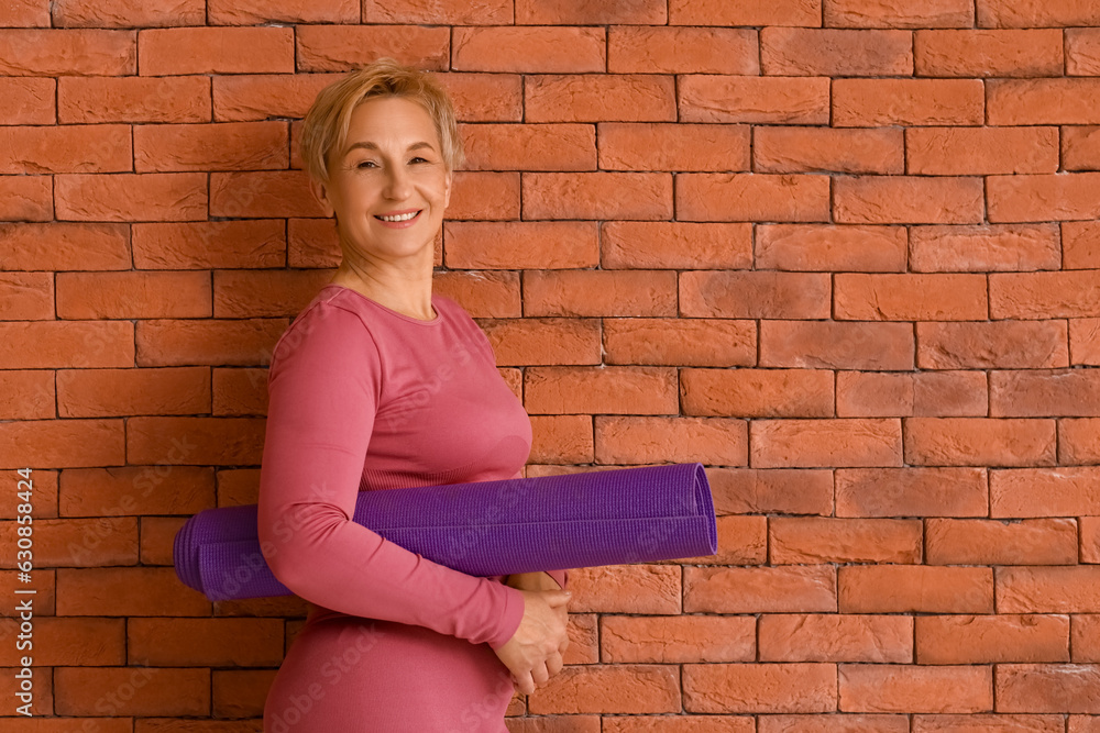 Mature woman with yoga mat near brick wall