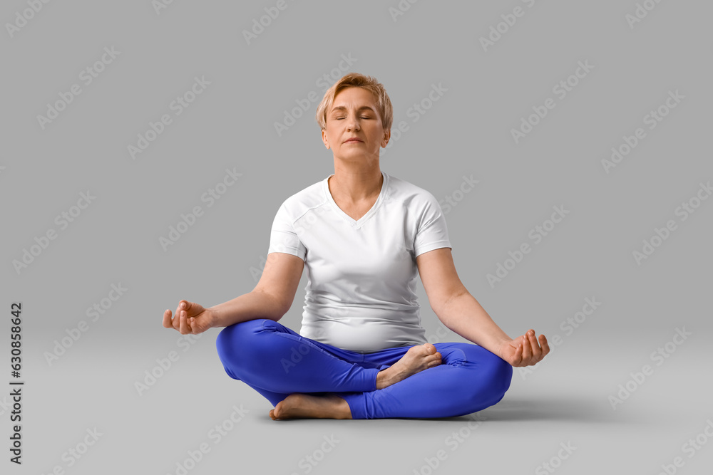 Sporty mature woman practicing yoga on light background