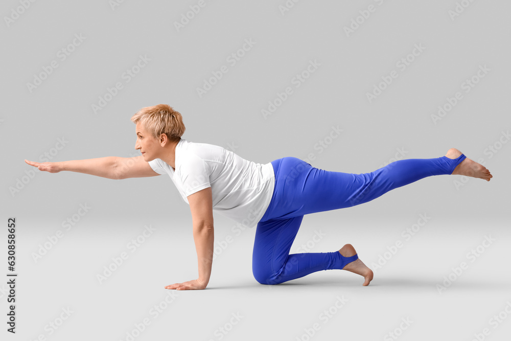 Sporty mature woman practicing yoga on light background