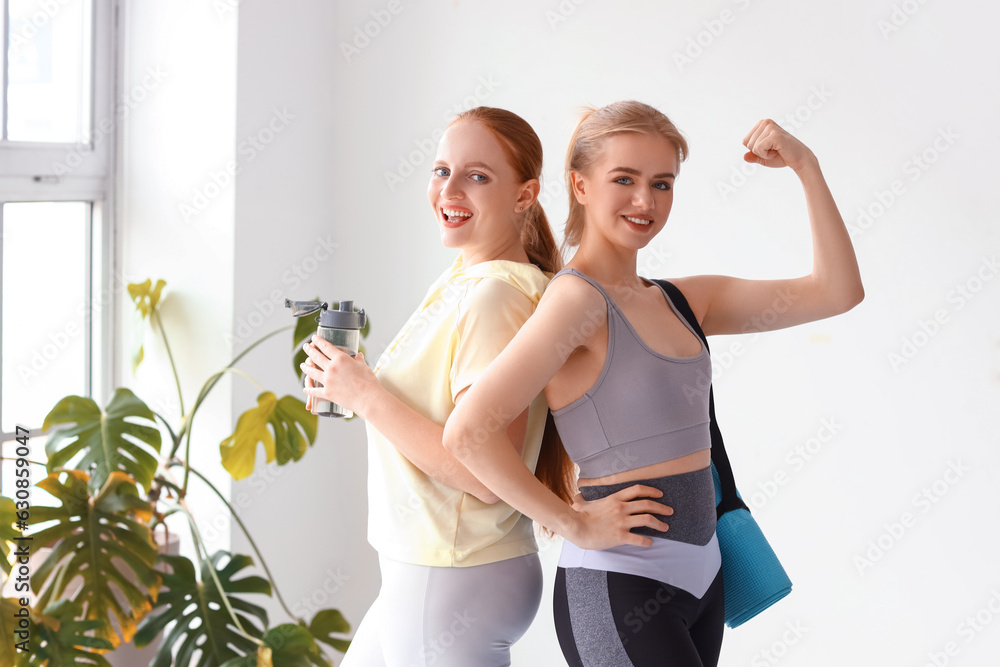 Portrait of sporty young women with bottle of water and yoga mat in gym