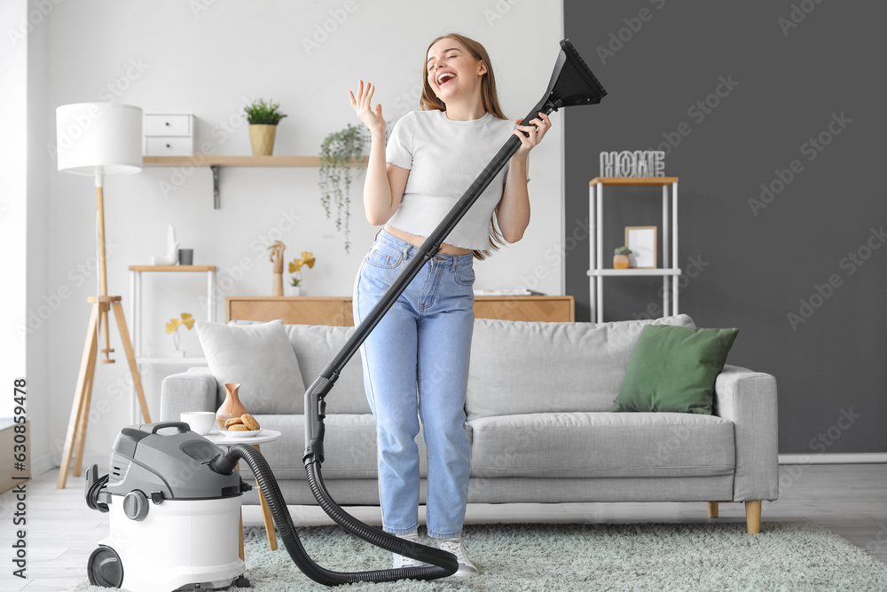 Young woman with vacuum cleaner singing at home