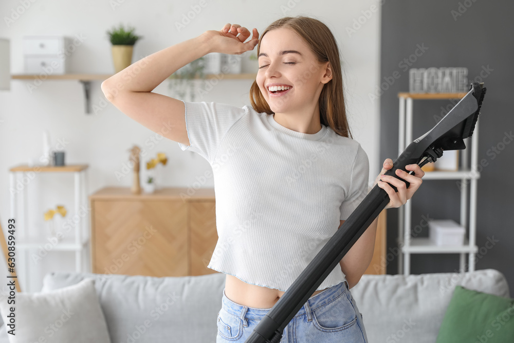 Young woman with vacuum cleaner singing at home