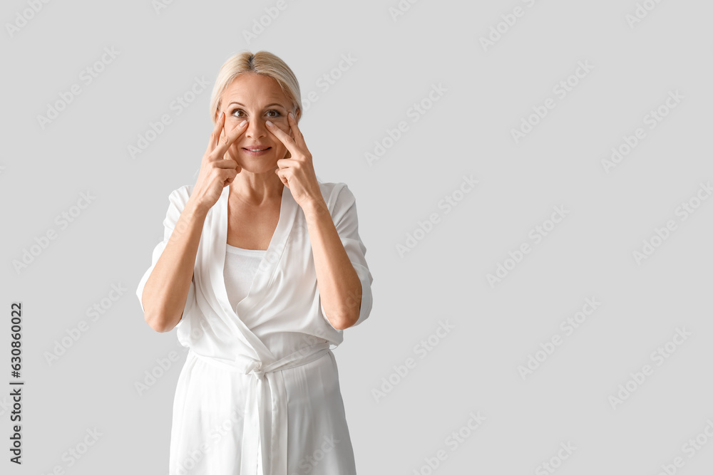 Mature woman doing face building exercise on light background