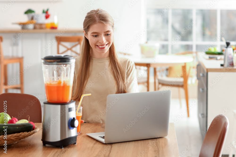 Young woman with healthy smoothie using laptop in kitchen