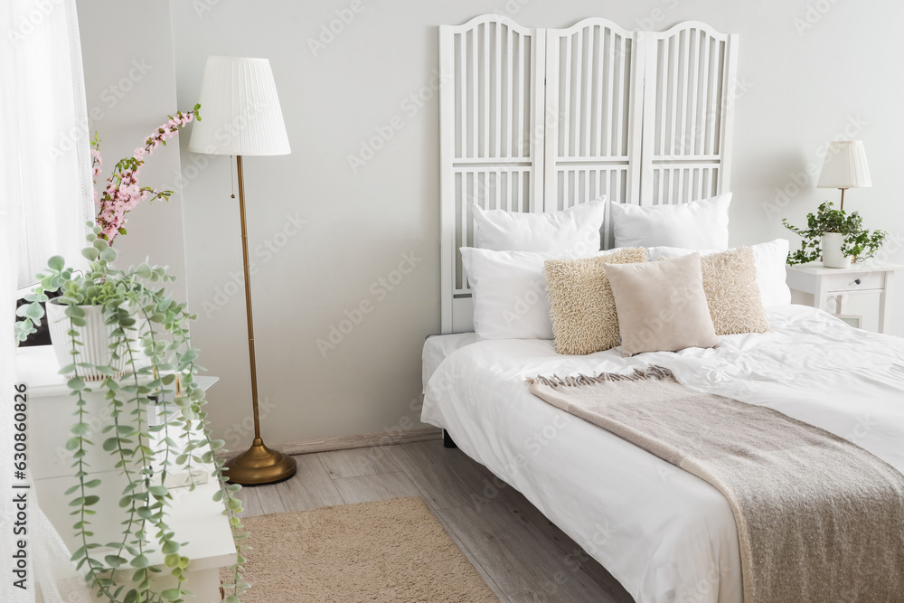 Interior of light bedroom with houseplants and blooming tree branches