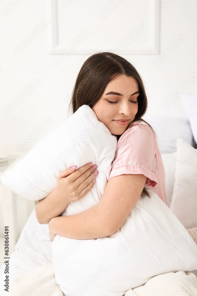 Pretty young woman with soft pillow sitting on bed