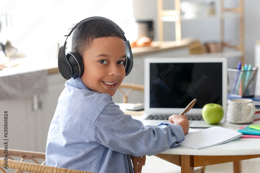 Little African-American boy in headphones studying computer sciences online at home