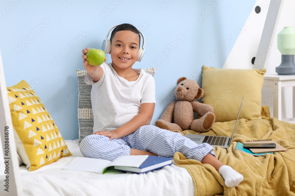 Little African-American boy with apple studying online in bedroom