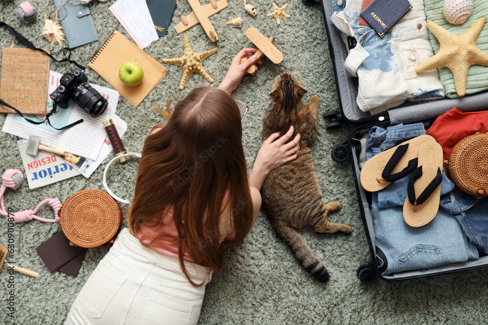 Woman with Scottish fold cat and travelling accessories on green carpet, top view