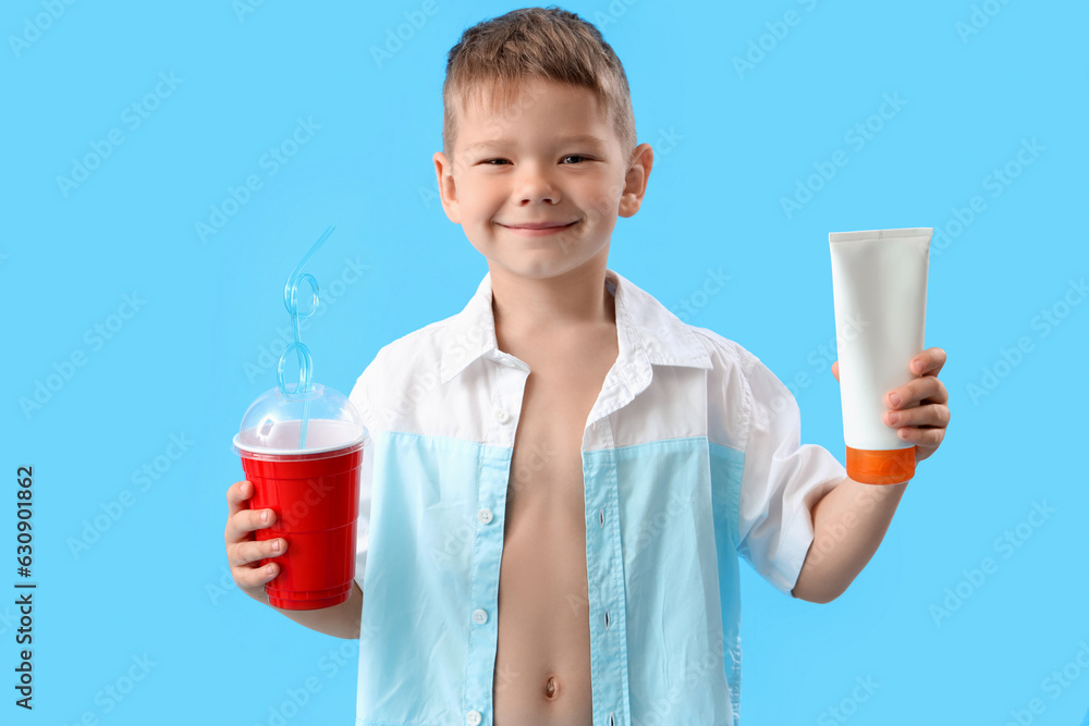 Little boy with bottle of sunscreen cream and cup of soda on blue background