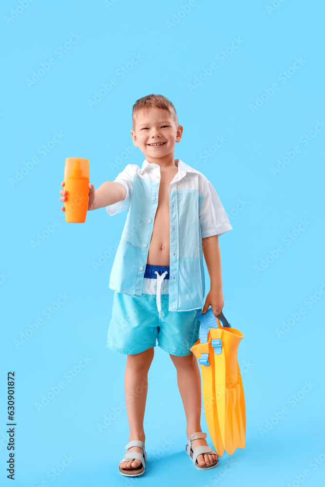 Little boy with bottle of sunscreen cream and flippers on blue background