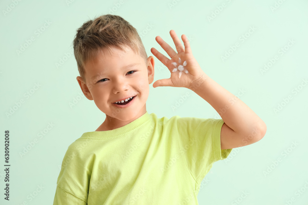 Little boy showing palm with sunscreen cream on pale green background