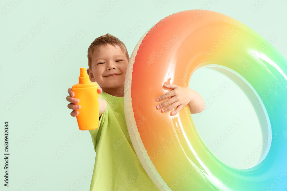 Little boy with bottle of sunscreen cream and inflatable ring on pale green background